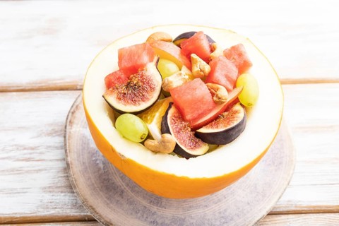 Vegetarian fruit salad of watermelon, grapes, figs, pear, orange, cashew on white wooden background