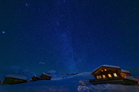 Mountain huts at night under a clear starry sky with illuminated windows in winter, Belalp, Naters,