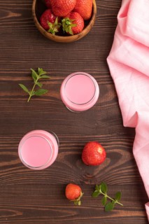 Sweet strawberry liqueur in glass on a brown wooden background and pink textile. top view, close