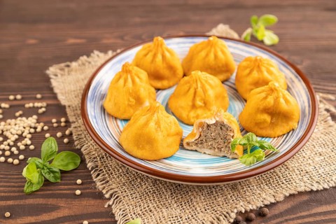 Fried manti dumplings with pepper, basil on brown wooden background and linen textile. Side view,