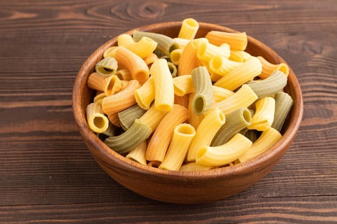 Rigatoni colored raw pasta with tomato, eggs, spices, herbs on brown wooden background. Side view,
