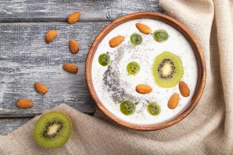 Yogurt with kiwi, gooseberry, chia and almonds in wooden bowl on gray wooden background and linen