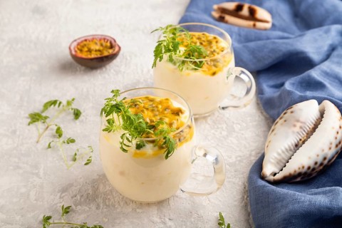 Yogurt with passionfruit and marigold microgreen in glass on gray concrete background with blue