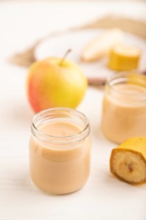 Baby puree with fruits mix, apple, banana infant formula in glass jar on white wooden background.