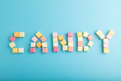The inscription candy laid out with various fruit jelly chewing candies on blue pastel background.