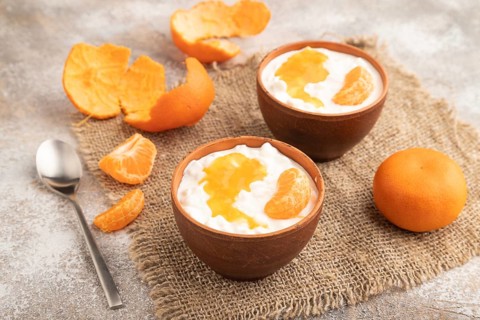 Grained cottage cheese with tangerine jam on brown concrete background and linen textile. side
