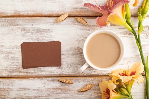 Brown paper business card mockup with orange day-lily flower and cup of coffee on white wooden