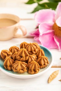 Homemade soft caramel fudge candies on blue plate and cup of coffee on gray concrete background,