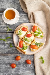White bread sandwiches with cream cheese, tomatoes and microgreen on gray wooden background and