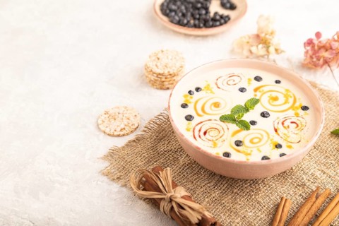 Yoghurt with bilberry and caramel in ceramic bowl on gray concrete background and linen textile.