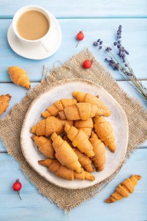 Homemade bagel roll with cup of coffee on a blue wooden background and linen textile. top view,