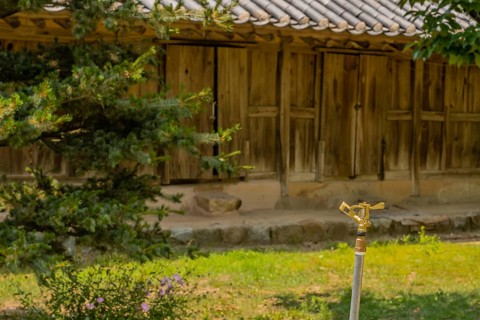 Copper water sprinkler in grassy lawn in front of wooden building located in public park displaying