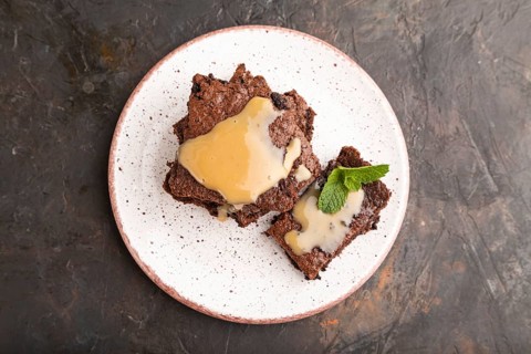 Chocolate brownie with caramel sauce with a cup of coffee on black concrete background. top view,