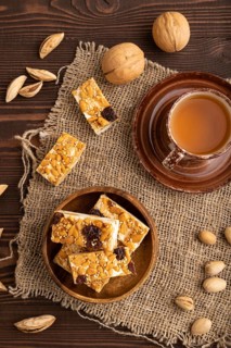 Traditional candy nougat with nuts and sesame with cup of green tea on brown wooden background and