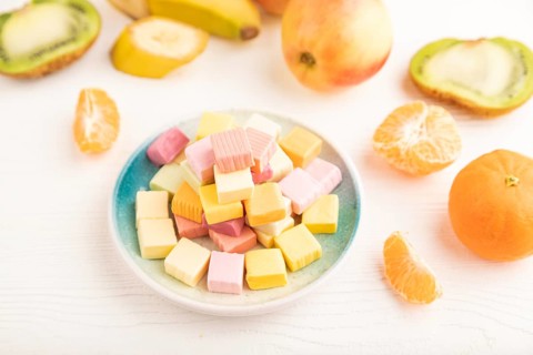 Various fruit jelly chewing candies on plate on white wooden background. apple, banana, tangerine,