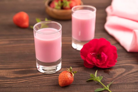 Sweet strawberry liqueur in glass on a brown wooden background and pink textile. side view, close