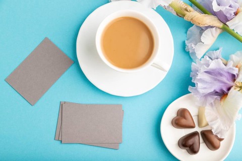 Gray business card with cup of cioffee, chocolate candies and iris flowers on blue pastel