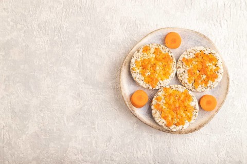 Carrot jam with puffed rice cakes on gray concrete background. Top view, flat lay, copy space
