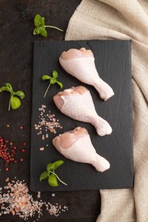 Raw chicken legs with herbs and spices on a black slate cutting board on a black concrete
