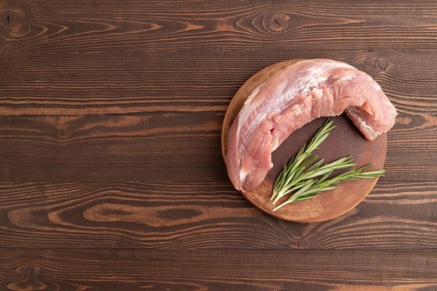 Raw pork with herbs and spices on a wooden cutting board on a brown wooden background. Top view,