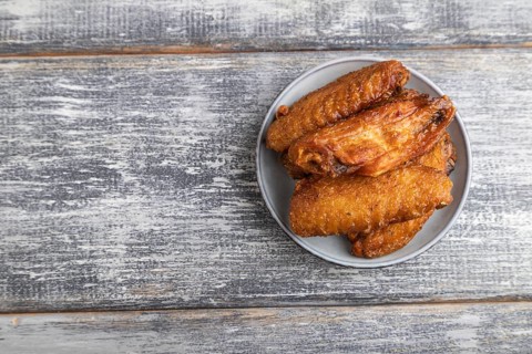 Fried chicken wings on a wooden plate on a gray wooden background. Top view, flat lay, close up,