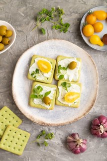 Green cracker sandwiches with cream cheese and cherry tomatoes on gray concrete background. top