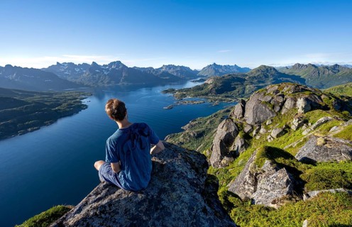 Mountaineer sitting on the summit of Dronningsvarden or Stortinden, behind mountains and fjord