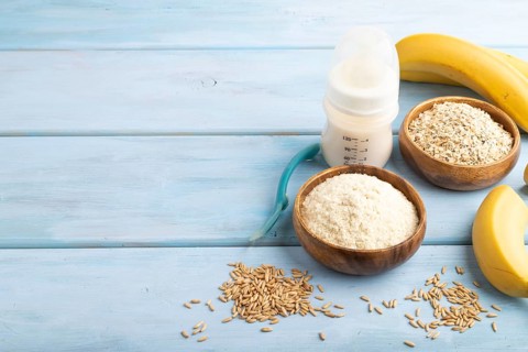 Powdered milk and oatmeal, banana baby food mix, infant formula, pacifier, bottle, spoon on blue
