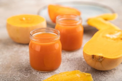 Baby puree with fruits mix, pumpkin, persimmon, mango infant formula in glass jar on brown concrete