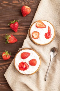 Grained cottage cheese with strawberry jam on brown wooden background and linen textile. top view,