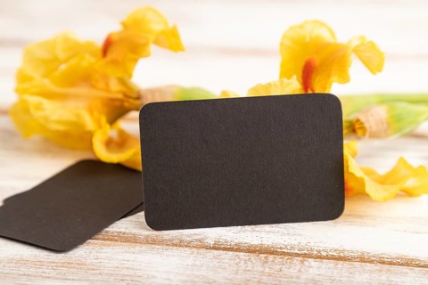 Black business card with iris yellow flowers on white wooden background. side view, copy space,