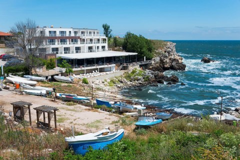 A hotel on the rocky coast with a view of the sea and several boats moored on the beach, harbour