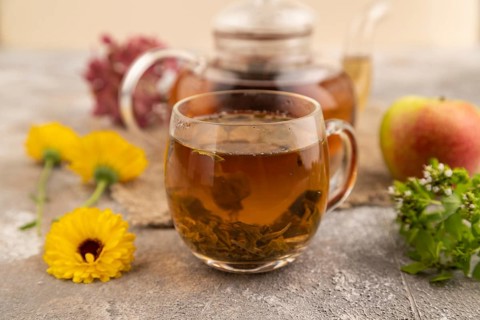 Red tea with herbs in glass teapot on brown concrete background and linen textile. Healthy drink