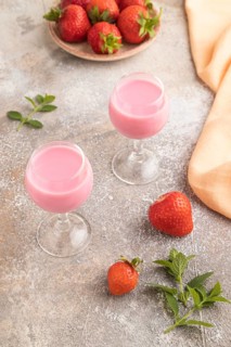 Sweet strawberry liqueur in glass on a gray concrete background and orange textile. side view,