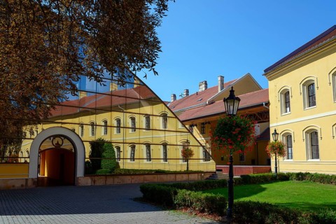 A yellow building reflected in a large glass facade, flanked by trees and a paved path, Officers'