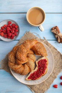 Homemade sweet bun with raspberry jam and cup of coffee on a blue wooden background and linen