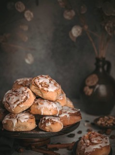 Homemade cinnamon buns surrounded by nuts, sultanas and cinnamon sticks on a dark background