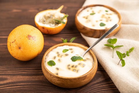 Yoghurt with granadilla and mint in wooden bowl on brown wooden background and linen textile. side