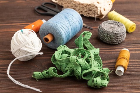 Sewing accessories: scissors, thread, thimbles, braid on brown wooden background. Side view, close