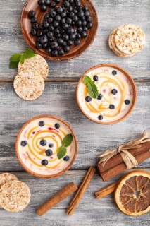 Yoghurt with bilberry and caramel in clay bowl on gray wooden background. top view, flat lay, close