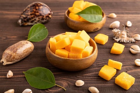 Dried and candied mango cubes in wooden bowls on brown wooden textured background. Side view, close
