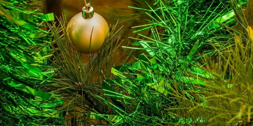 Closeup of gold Christmas ornament and green tensile garland hanging on pine tree in local park in