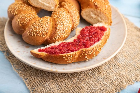 Homemade sweet bun with raspberry jam and cup of coffee on a blue wooden background and linen