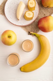 Baby puree with fruits mix, apple, banana infant formula in glass jar on white wooden background.