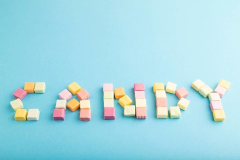 The inscription candy laid out with various fruit jelly chewing candies on blue pastel background.