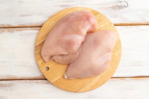 Raw chicken breast with herbs and spices on a wooden cutting board on a white wooden background.