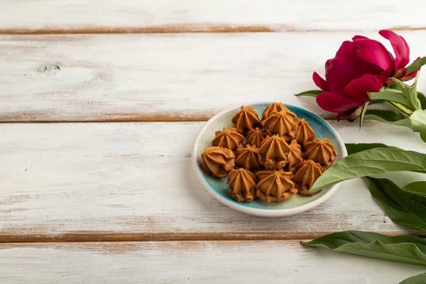 Homemade soft caramel fudge candies on blue plate on white wooden background, peony flower