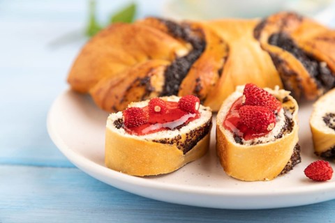 Homemade sweet bun with strawberry jam and cup of green tea on a blue wooden background. side view,