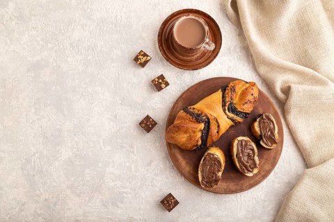 Homemade sweet bun with chocolate cream and cup of coffee on a gray concrete background and linen
