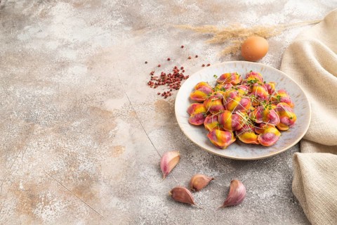 Rainbow colored dumplings with pepper, herbs, microgreen on brown concrete background and linen